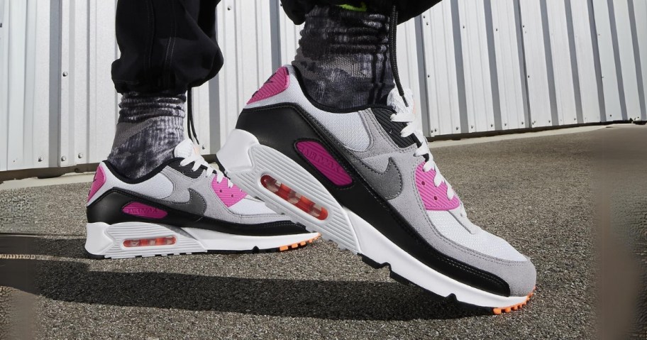 man's legs and feet wearing black Nike pants, black and white Nike socks, and black, white, grey and pink Nike Air Max shoes 