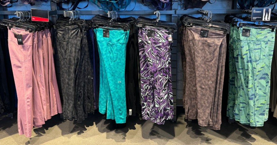 clothing display in store with women's Under Amrour leggings in various solid colors and prints hanging from a wall display