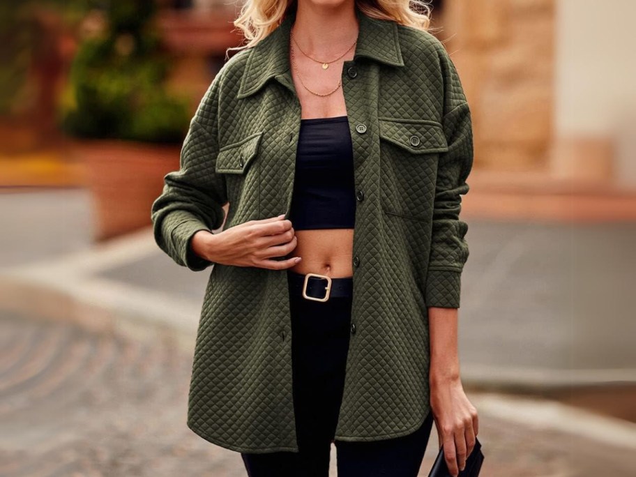 woman standing outside a building wearing a green quilted shacket with a black crop top and black jeans