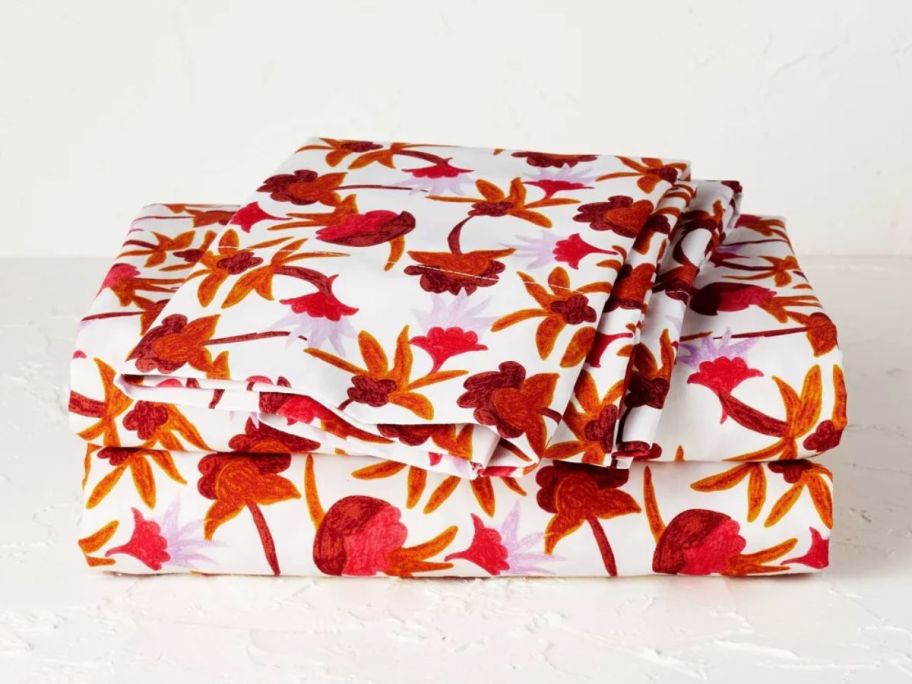 set of sheets white with red and orange flowers stacked on a bed