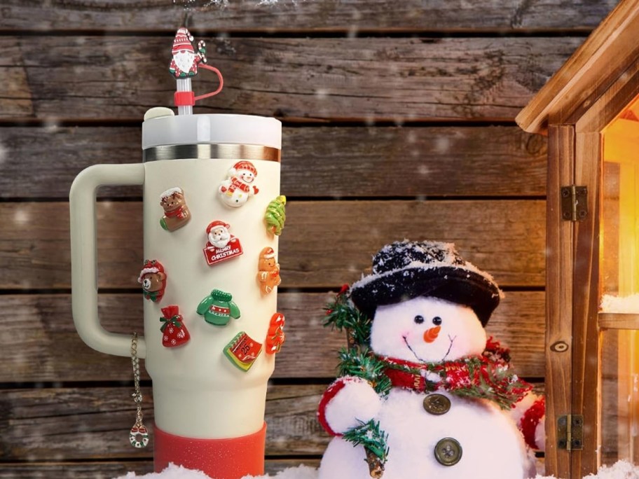 a cream color Stanley Tumbler with Christmas accessories on it sitting next to a plush snowman