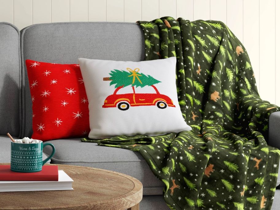 a christmas tree print blanket draped over a sofa and shown with throw pillows