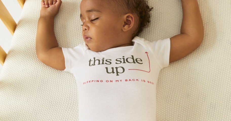 a baby sleeping on it's back wearing a white short sleeve onesie that says "this side up"