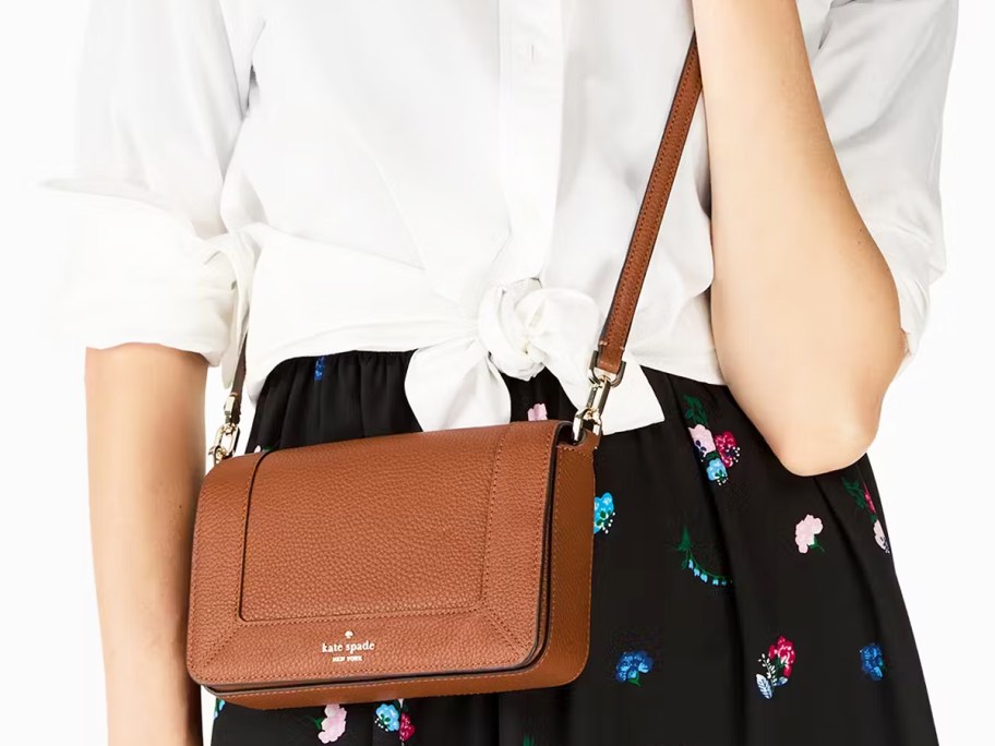 woman in white top and black floral skirt with a brown crossbody bag