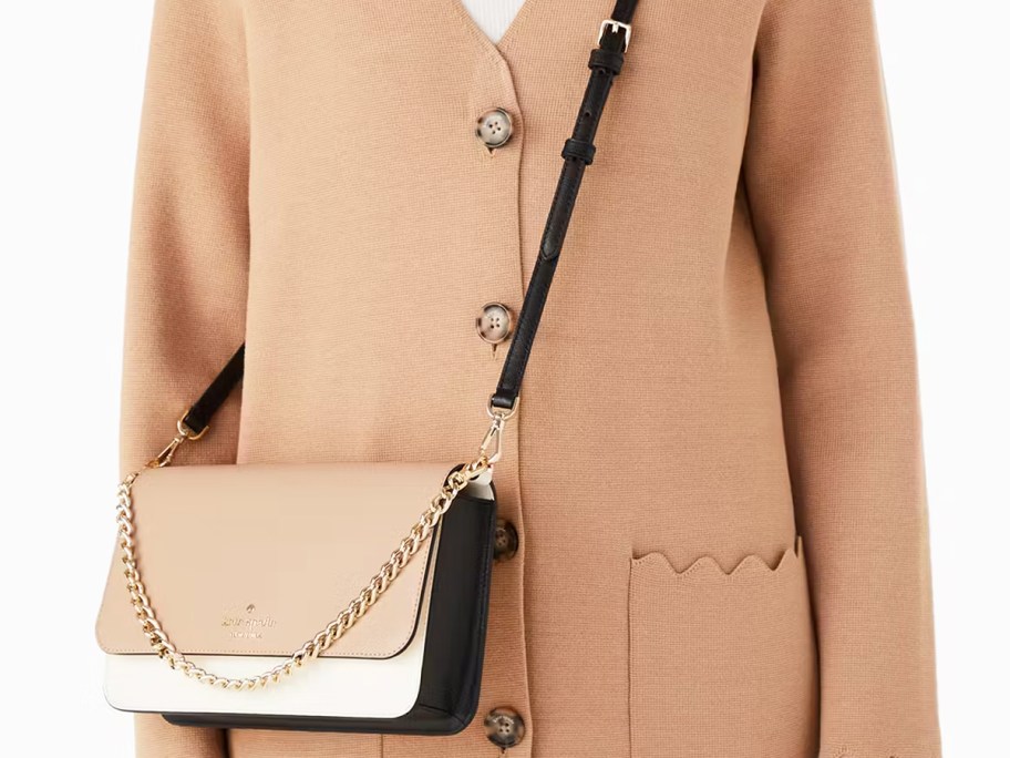 woman in tan coat with a tan, white, and black crossbody bag