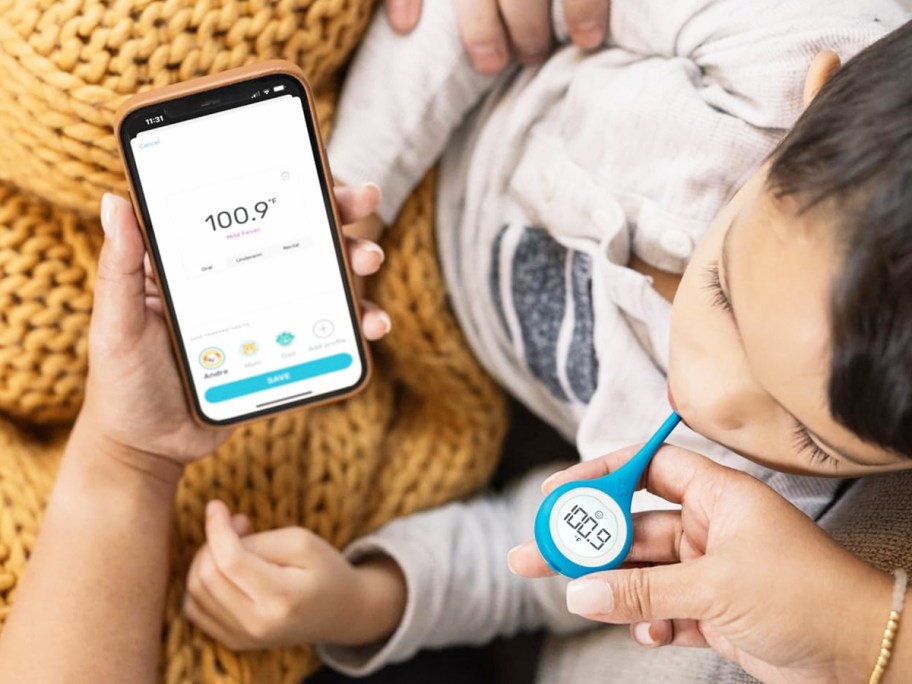 woman taking child's temperature with thermometer and phone app