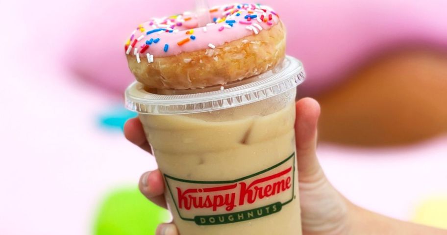 Hand holding a Krispy Kreme Iced Coffee with a spinkled doughnut with pink icing on top of it