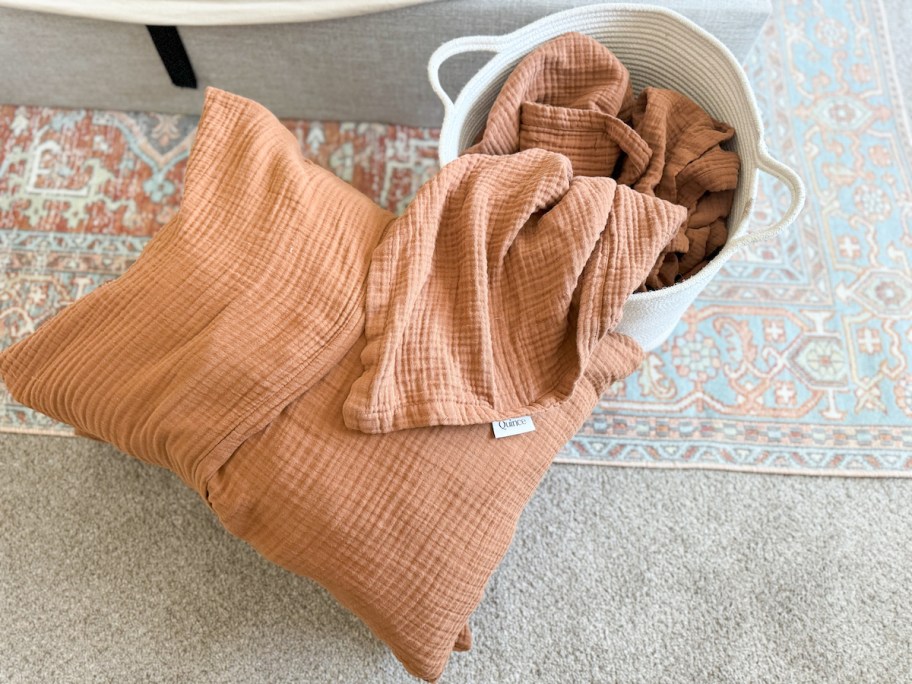 orange gauze pillow and blanket on floor and in basket