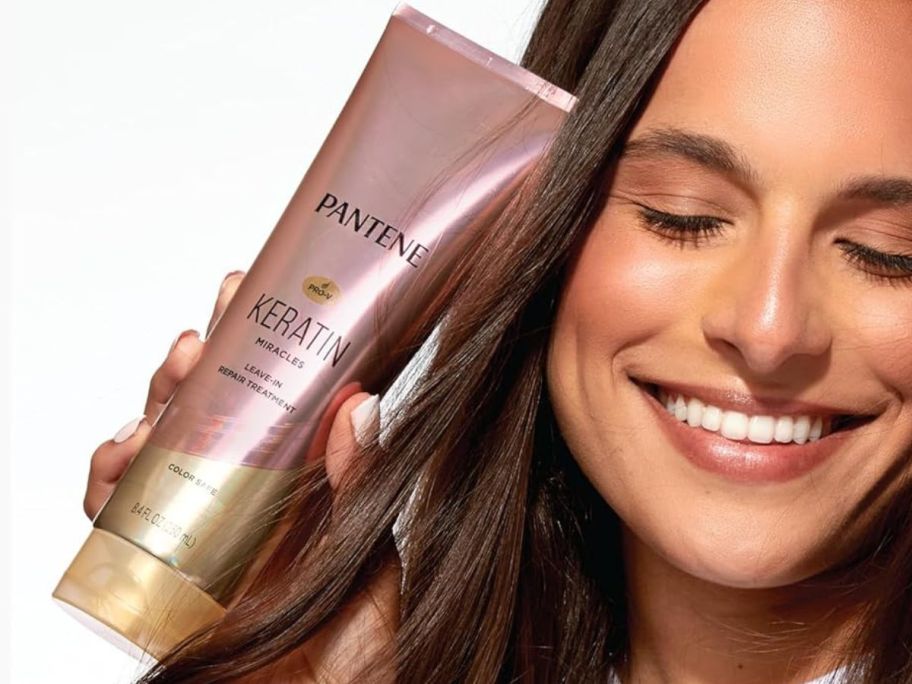 A woman holding a Pantene Keratin Miracles Leave-In Treatment tube