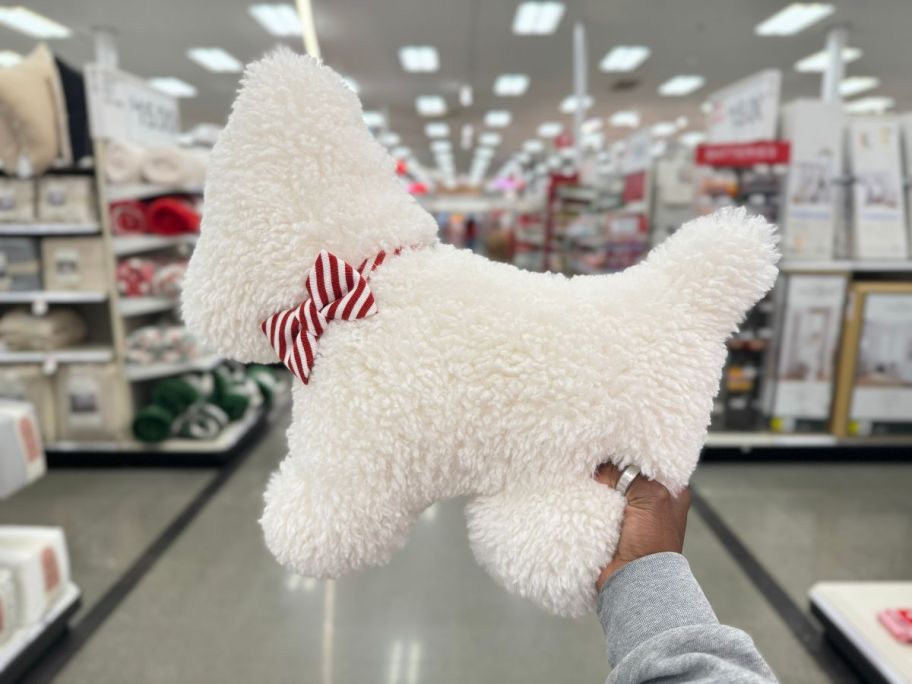 a womans hand holding a dog shaped holiday throw pillow
