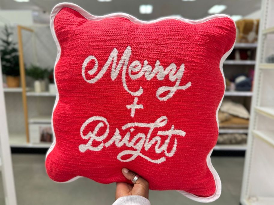 Hand holding up a red Threshold Woven Square Throw Pillow w/ Scalloped Trim with the words Merry & Bright on it