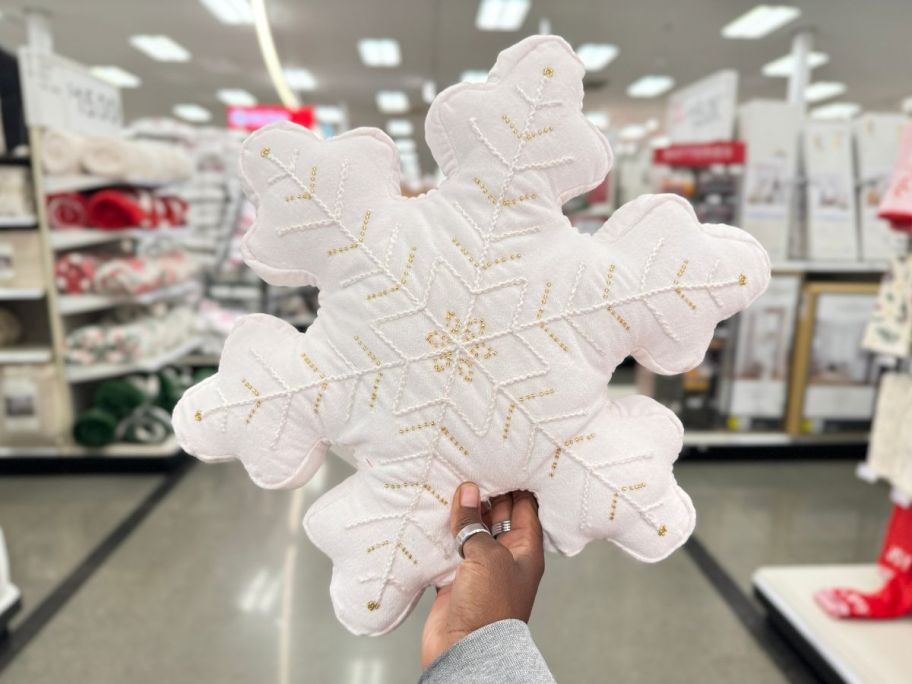 a womans hand holding a snowflake shaped holiday throw pillow