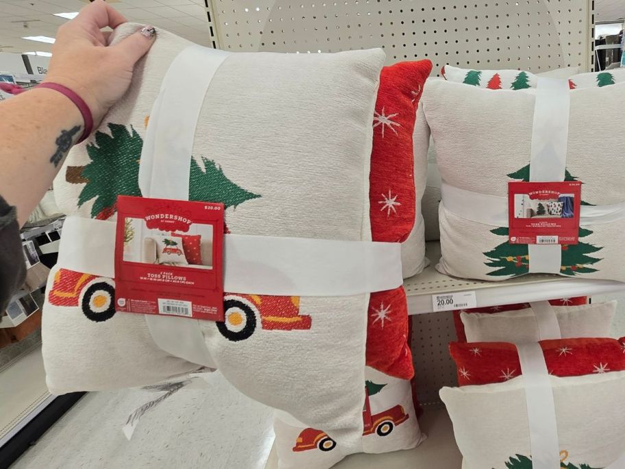 a womans hand holding a holiday throw pillow with a truck hauling a christmas tree on it 