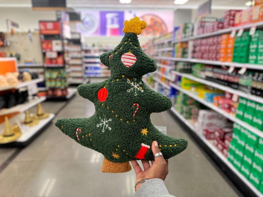 a womans hand holding a tree shaped holiday throw pillow