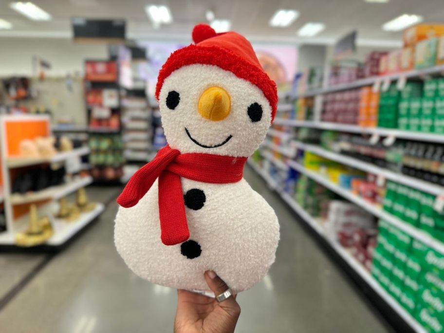 a womans hand holding a snowman shaped holiday throw pillow