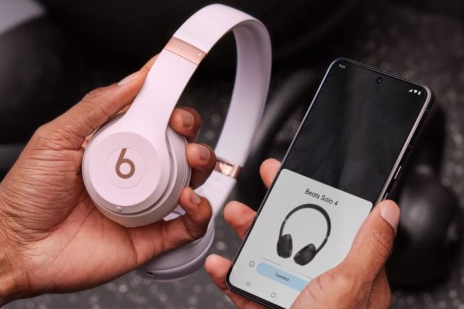 pink headphones next to phone in hand