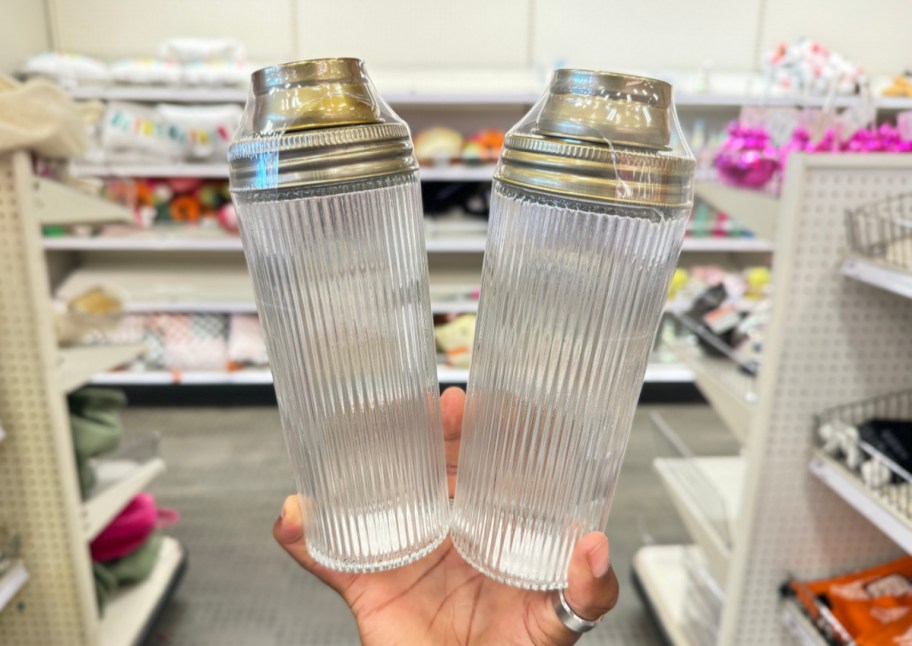 hand holding two clear and gold cocktail shakers