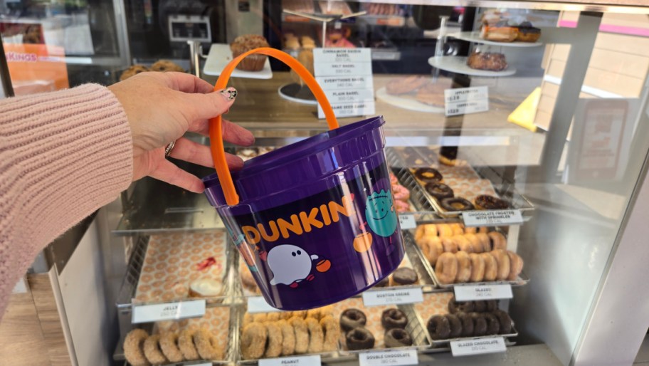 hand holding up the halloween dunkin munchkins bucket in front of a donut display in store