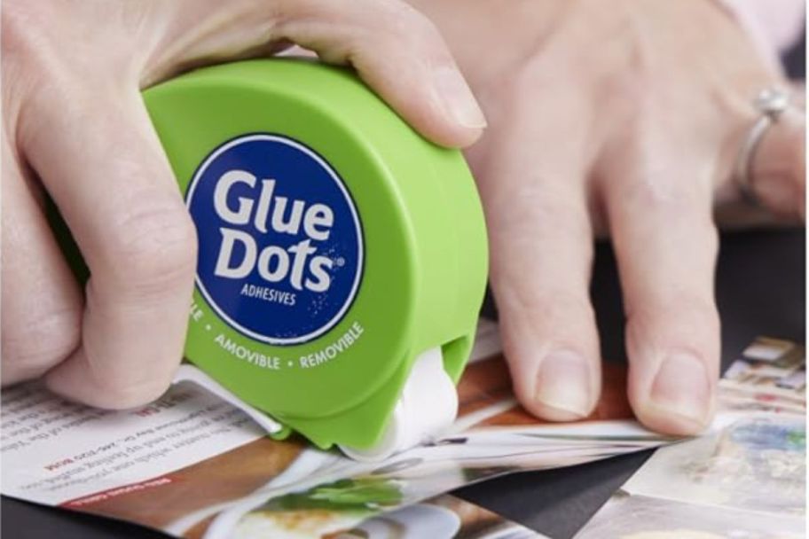 a hand holding a glue dots dispenser to a sheet of paper