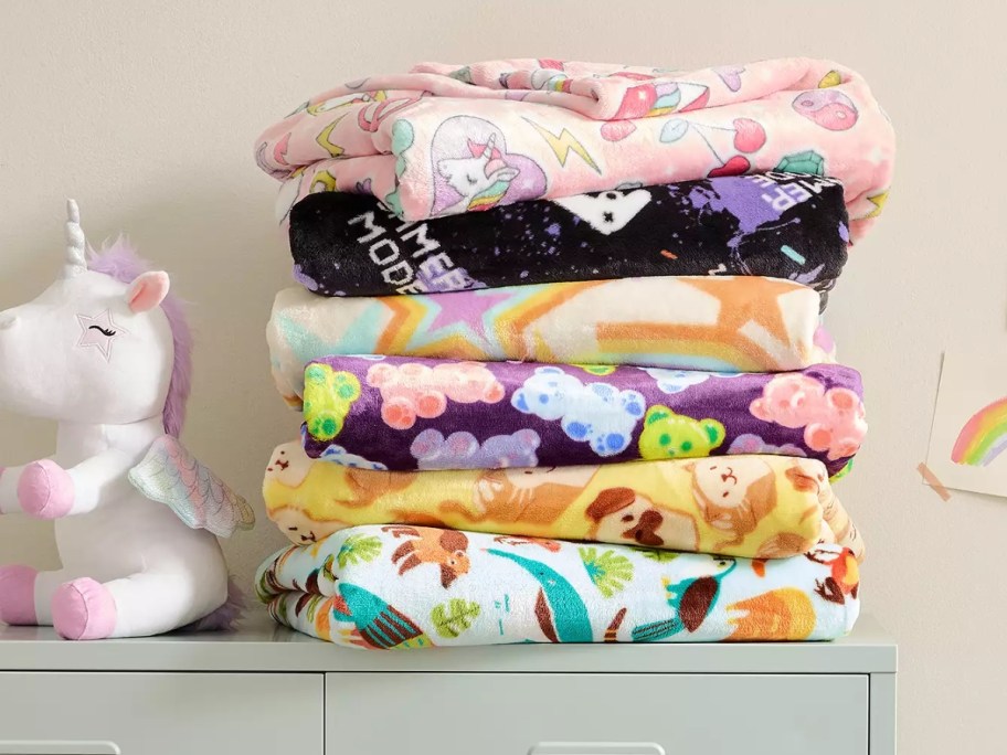 plush throw blankets in kids designs on top of a dresser next to a stuffed unicorn