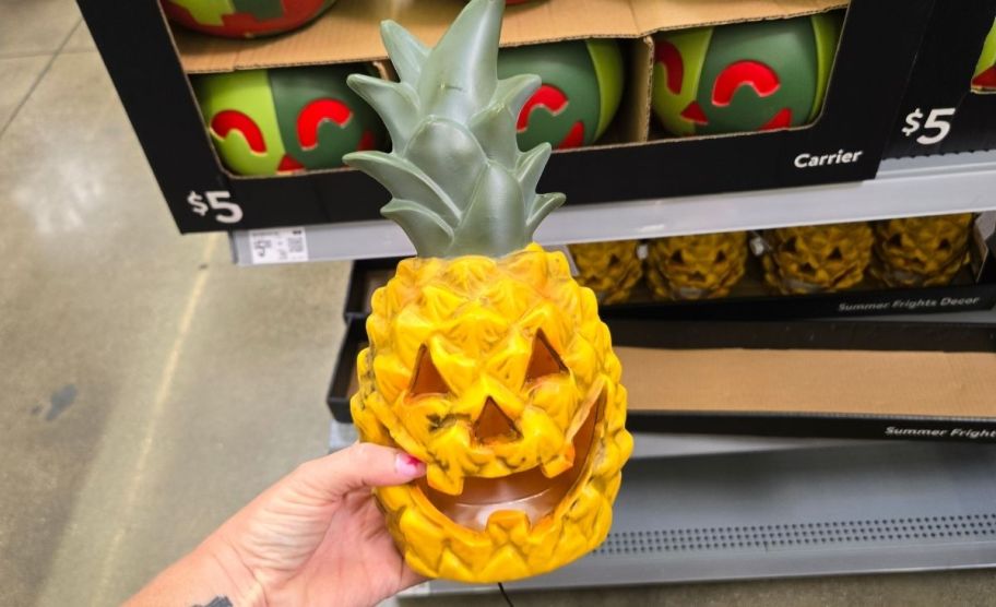 a woman's hand holding a lighted pineapple lanter