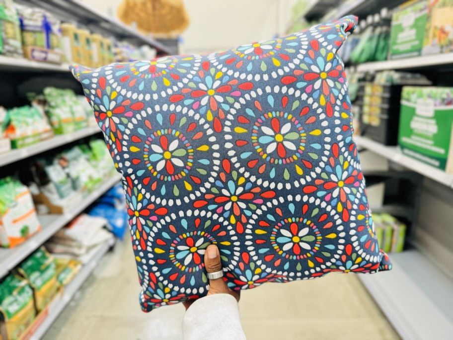 a womans hand holding up a medallion print throw pillow on a store aisle