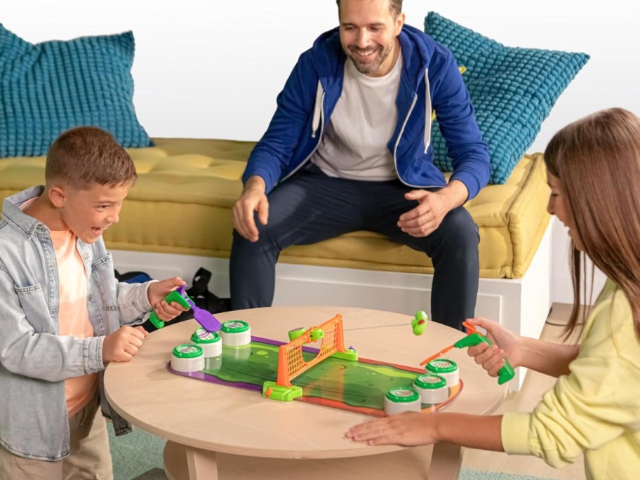 man, woman, and boy playing pickleball blast game at a coffee table in front of a couch