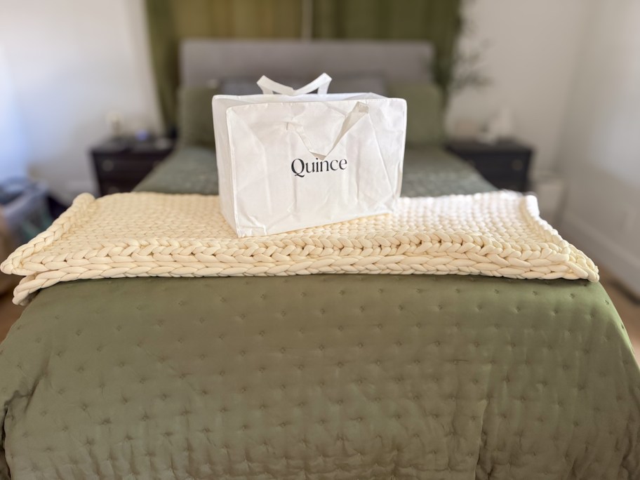 close up of edge of bed with green quilt and braided throw blanket with quince bedding bag on top