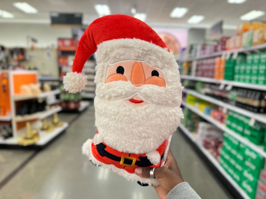 a womans hand holding a santa shaped holiday throw pillow