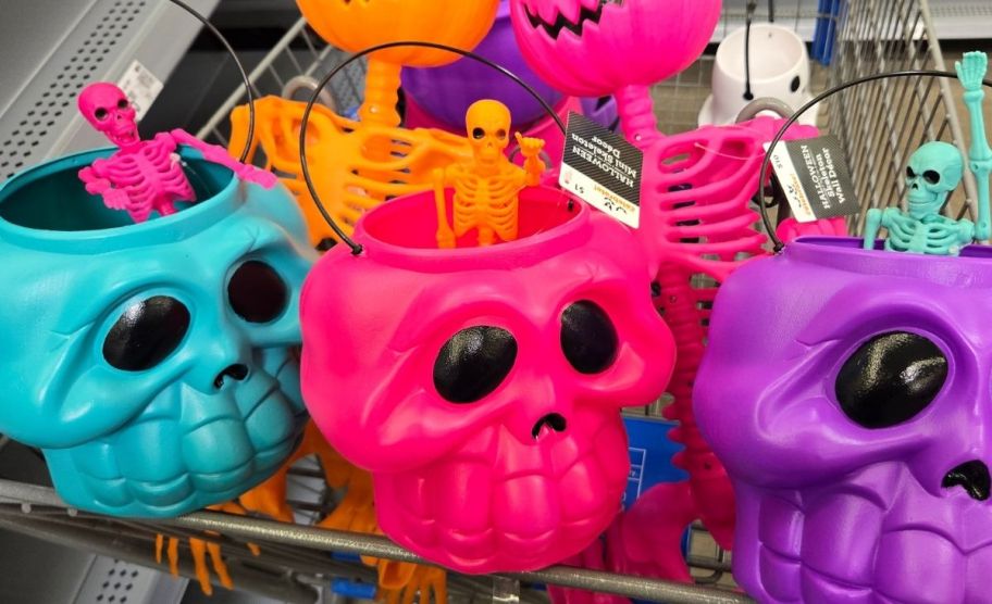 a shopping cart filled with neon skull treat pails, mini skellies, and pumpkin head skellies