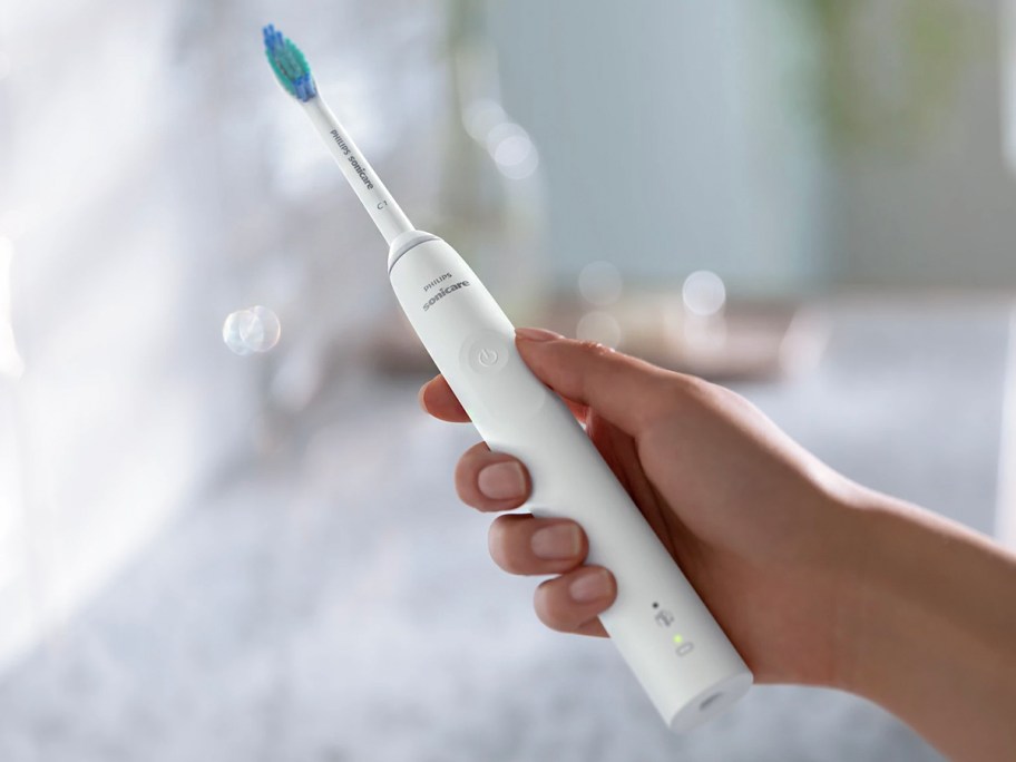 hand holding white sonic care toothbrush in bathroom 