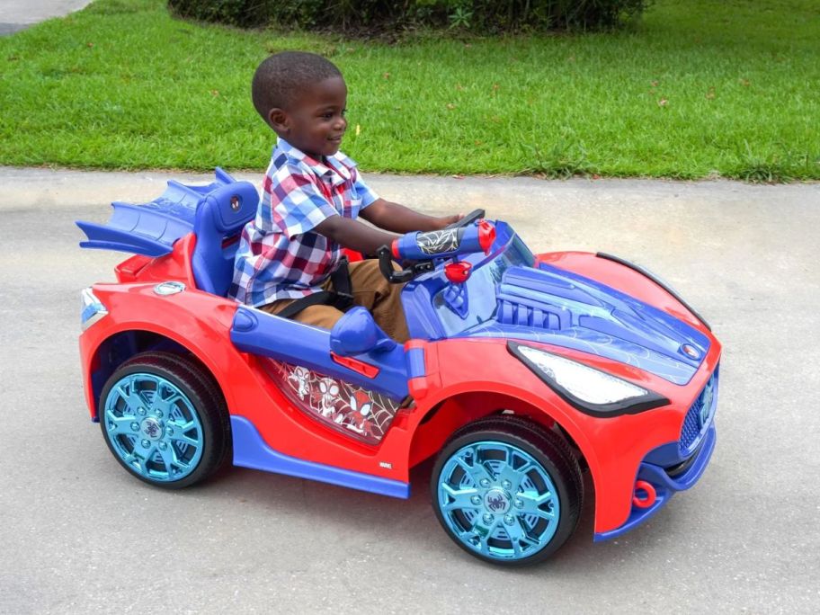 a little boy driving a spider man super car ride on in a driveway