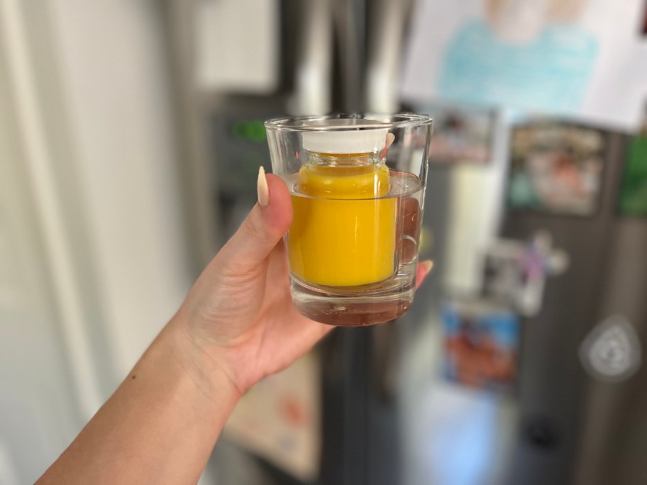 hand holding glass with mini shot glass with orange colored juice inside