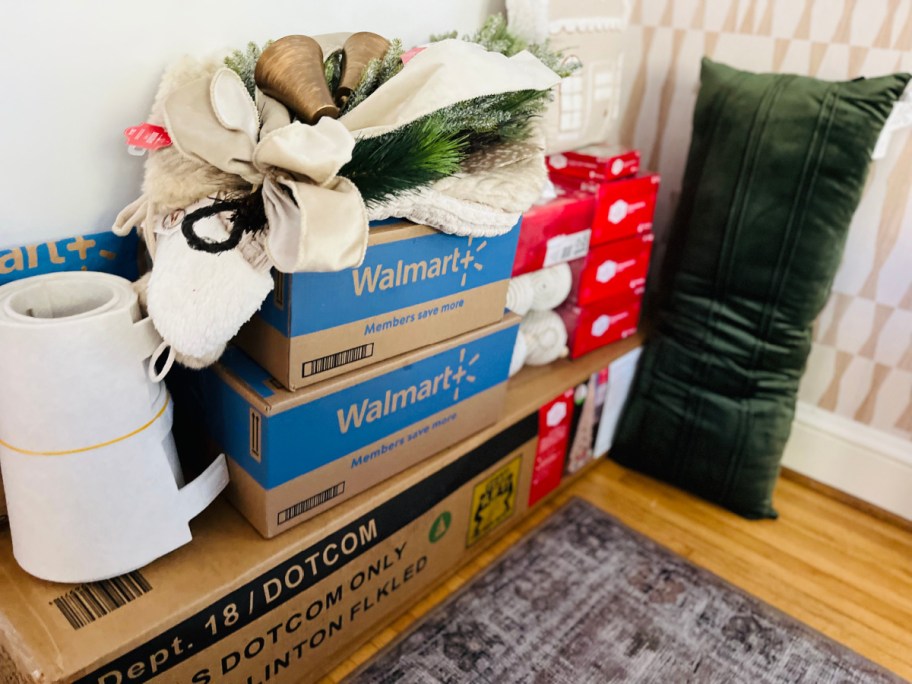boxes of Walmart Christmas decorations and decor stacked on a bench near a front door
