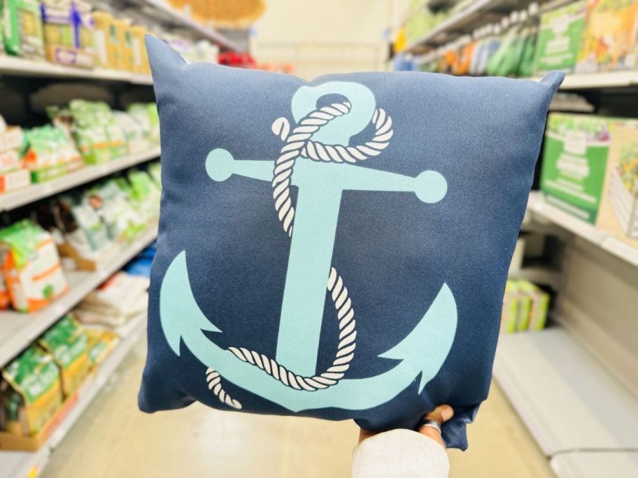 a womans hand holding up an anchor throw pillow on a store aisle