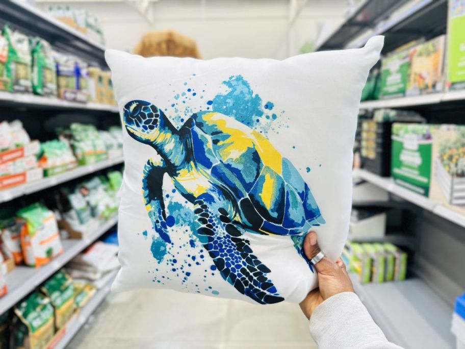 a womans hand holding up a sea turtle throw pillow on a store aisle