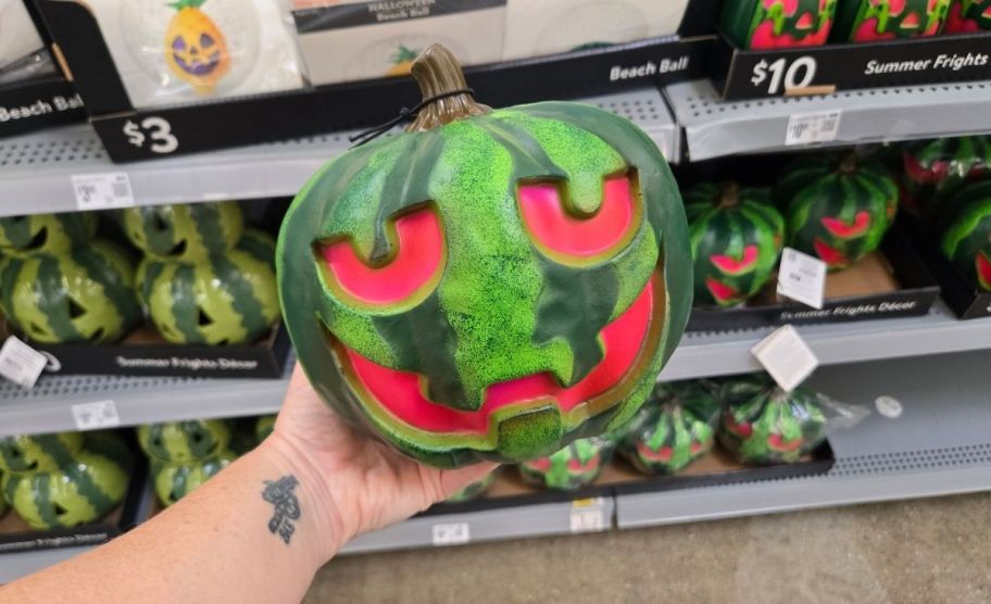 a woman's hand holding a watermelon jack o lantern