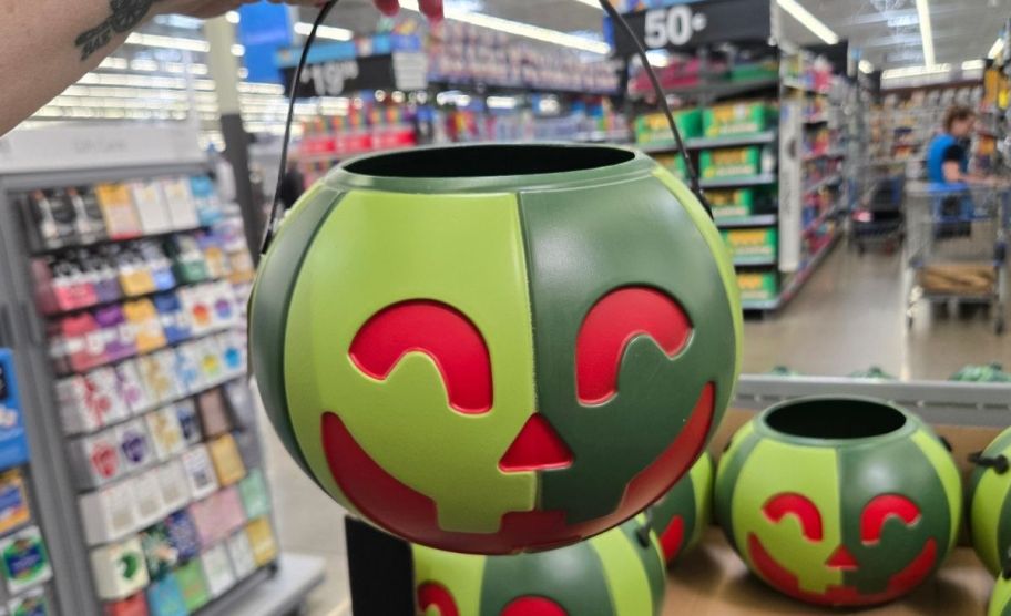 a woman's hand holding a watermelon jack o lantern treat pail