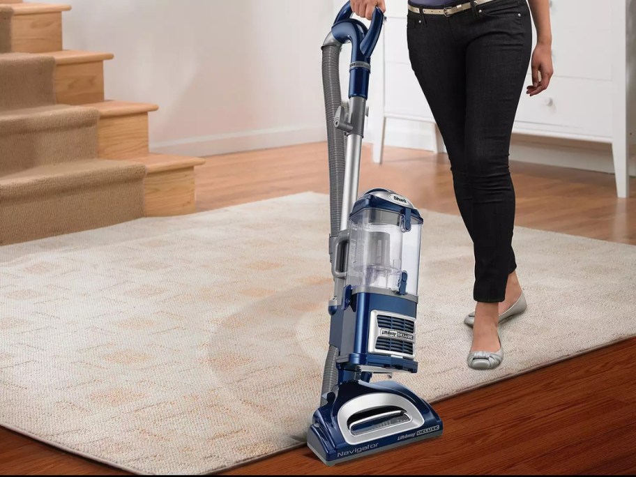 woman using a blue Shark vacuum to vacuum the floor in a living room
