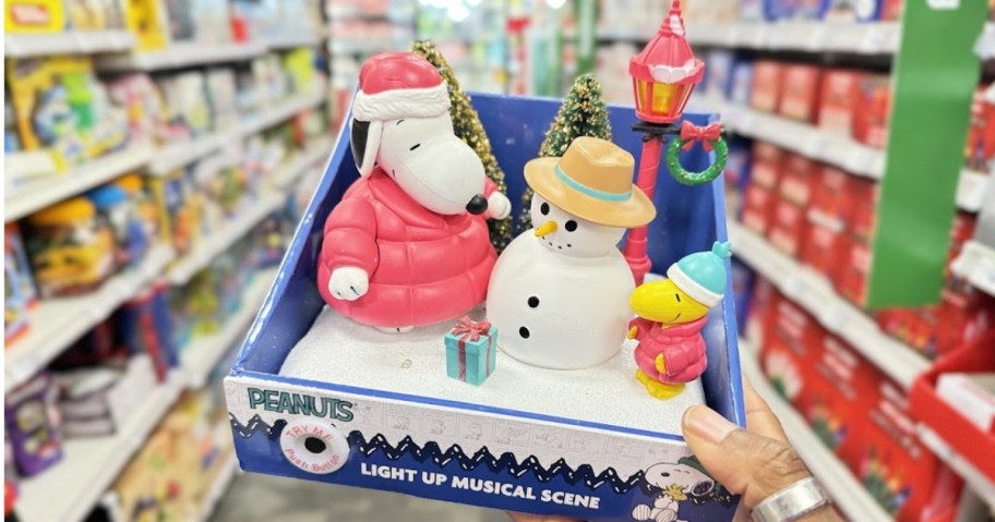 hand holding a holiday decor piece with Snoopy and Woodstock building a snowman, CVS aisle in the background