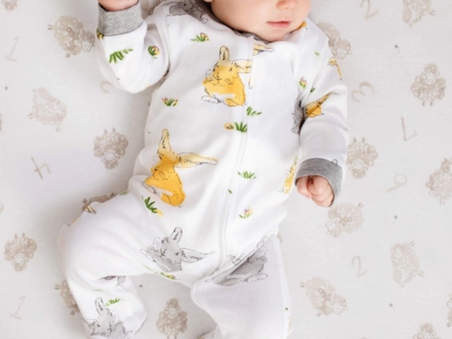 a baby in a white footed pajama with bunny rabbits on it, laying on a bed