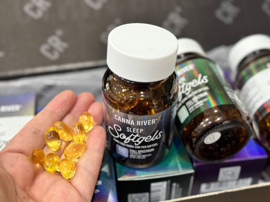 hand holding many Canna River Sleep softgels next to the bottle they came from
