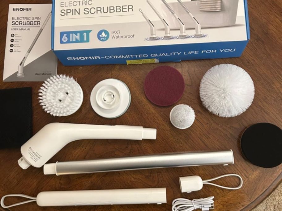ENOMIR Cordless Electric Spin Scrubber with the handle and attachments on a table next to the box