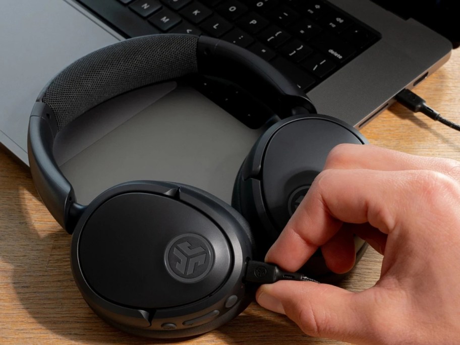 a pair of black Jlab wireless headphones with a person plugging them in to be charged