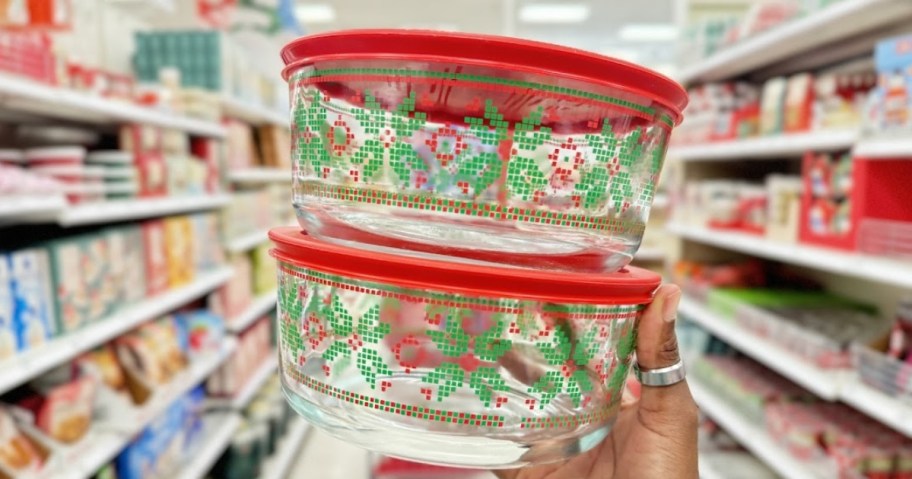 hand holding 2 glass Pyrex containers with Christmas sweater designs on them and red lids 