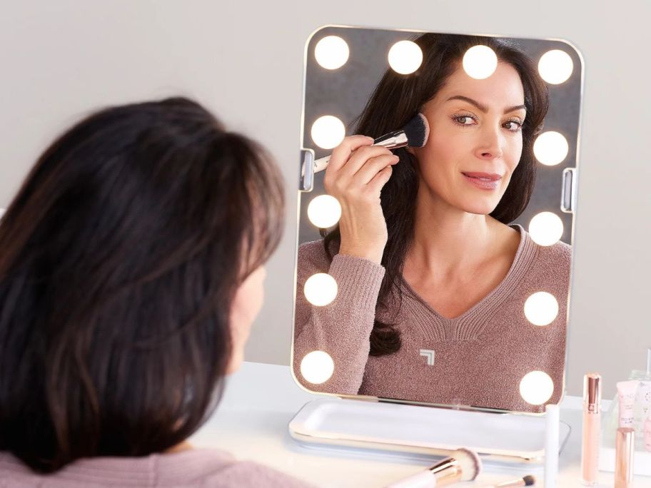 A woman looking at herself in the mirror while applying makeup 