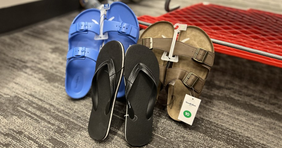 Three pairs of men’s sandals on display at Target, including blue slide sandals with double buckles, classic black flip-flops, and tan Goodfellow & Co. sandals with dual buckle straps