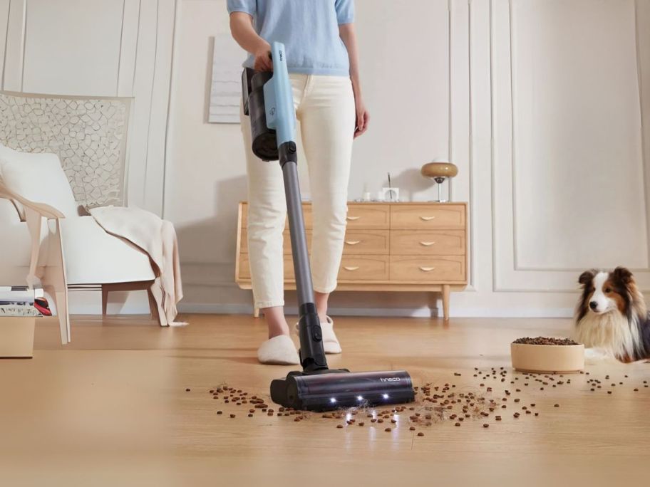 woman using Tineco GO Pet Cordless Stick Vacuum w/ ZeroTangle Brush Technology to vacuum up dog food off the floor