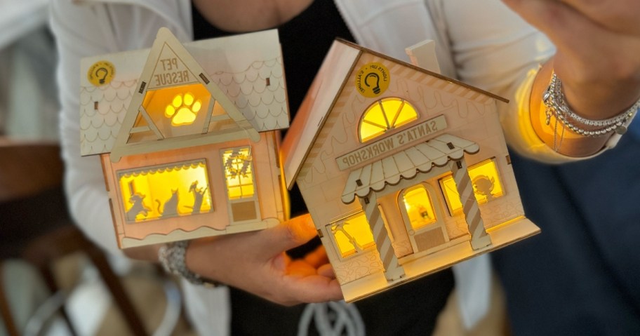 woman holding 2 wooden holiday craft houses that are lit up