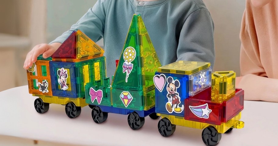 a little boy playing with a set of magnetic tiles he's made into a train, this set is Disney themed and has Mickey and Disney stickers on it